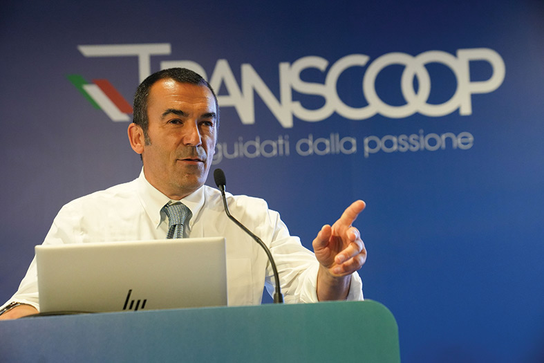 direttore generale di Transcoop che parla al microfono da un leggio con in sfondo la scritta Transcoop